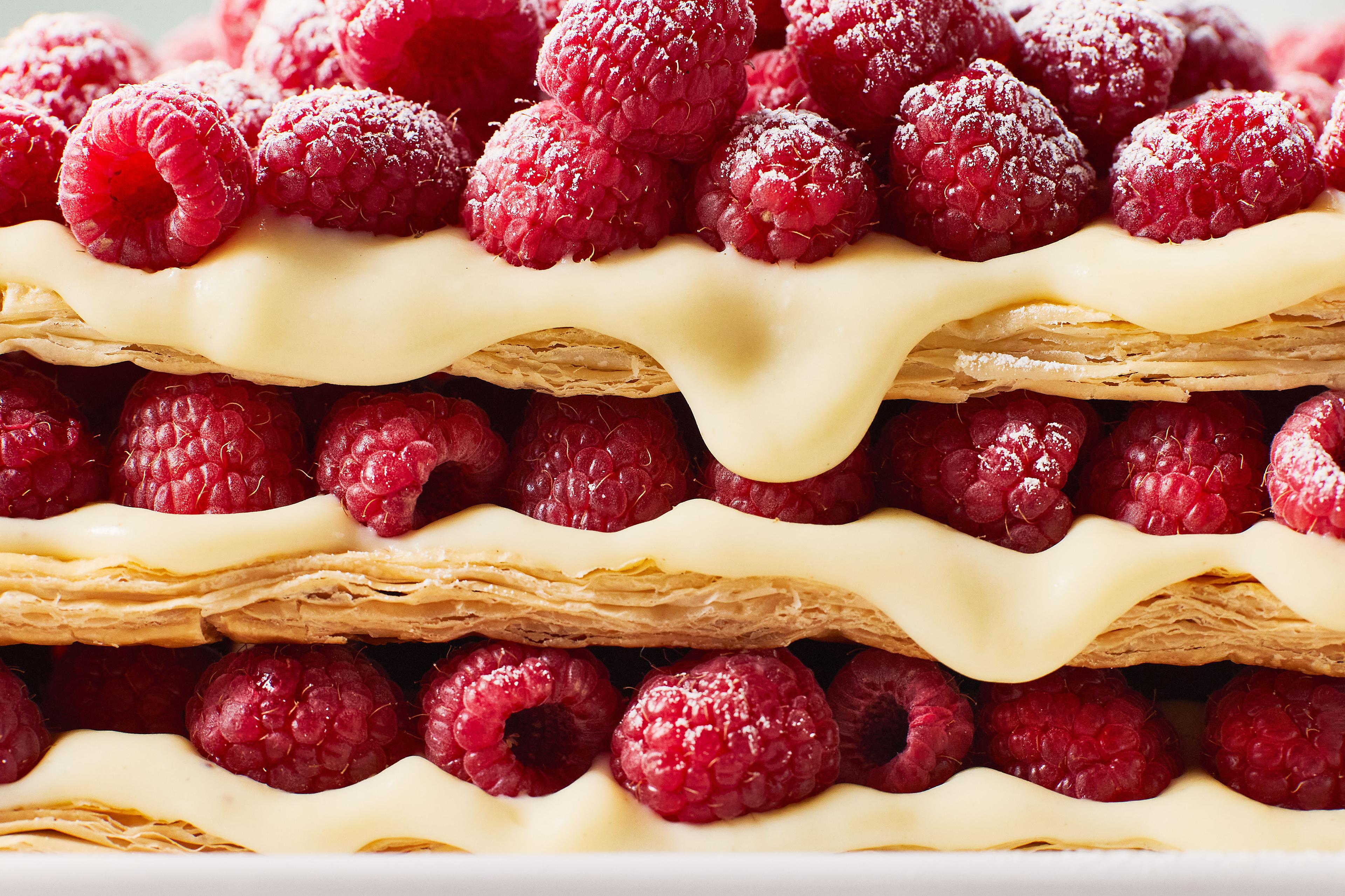 A delicious looking closeup of a raspberry puff pastry dessert with exquisitely and artfully dripping icing and some powdered sugar.